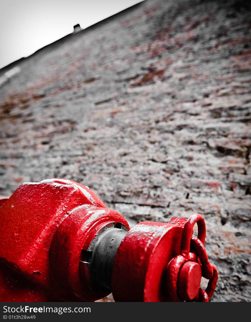 A red hydrant against high brick wall.