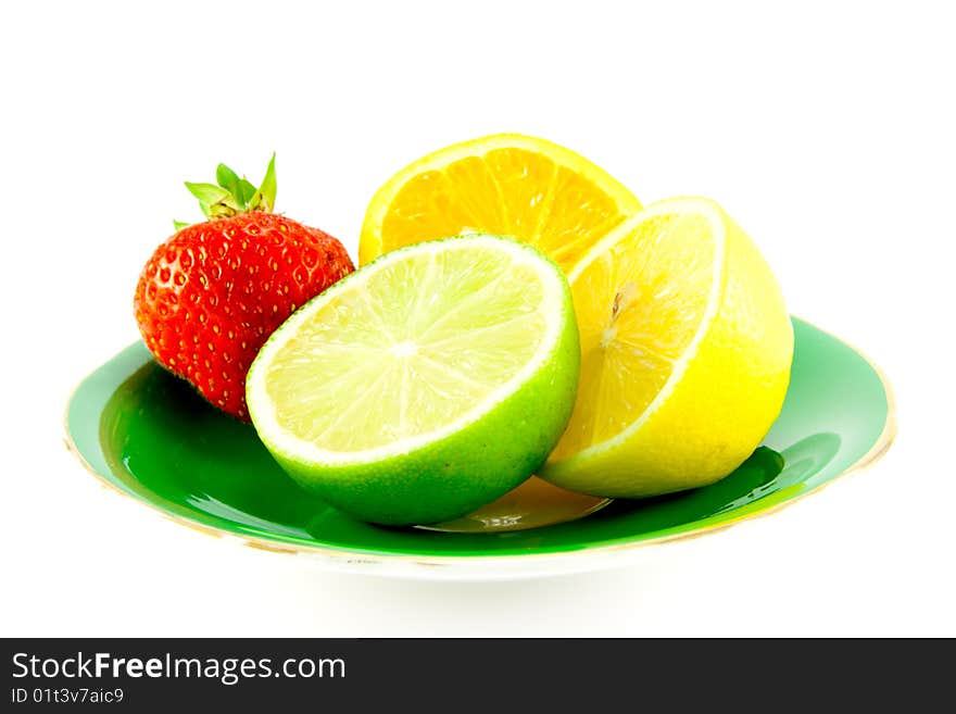 Lemon, lime and orange halves on a fancy green plate with a red juicy strawberry on a white background. Lemon, lime and orange halves on a fancy green plate with a red juicy strawberry on a white background