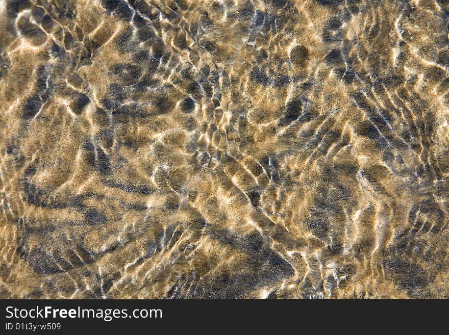 Closeup of clear water flowing over black and yellow sand forming patterns and ripples. Closeup of clear water flowing over black and yellow sand forming patterns and ripples