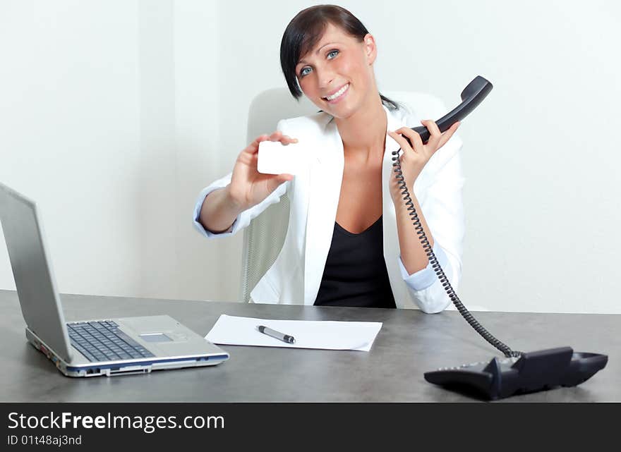 Office woman sitting and holding blank businesscard smiling on table and telephone