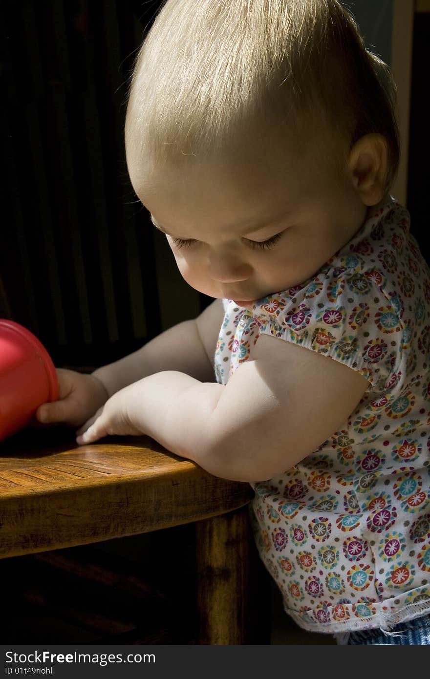 Candid photo of an infant girl staring downwards whilst leaning on a chair. Natural light from a window. Candid photo of an infant girl staring downwards whilst leaning on a chair. Natural light from a window