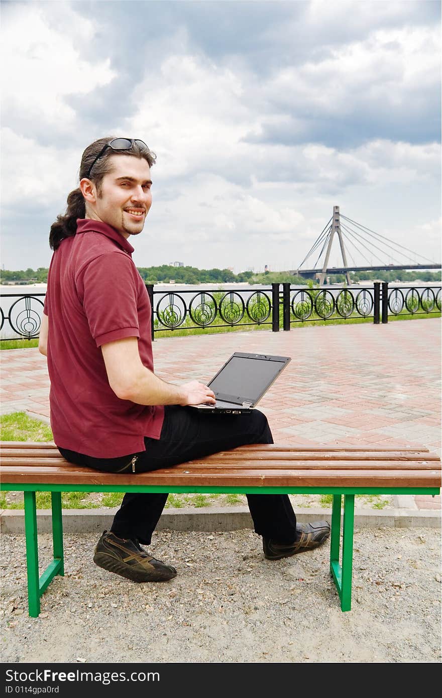 Young man sitting on a park bench with his laptop. Young man sitting on a park bench with his laptop