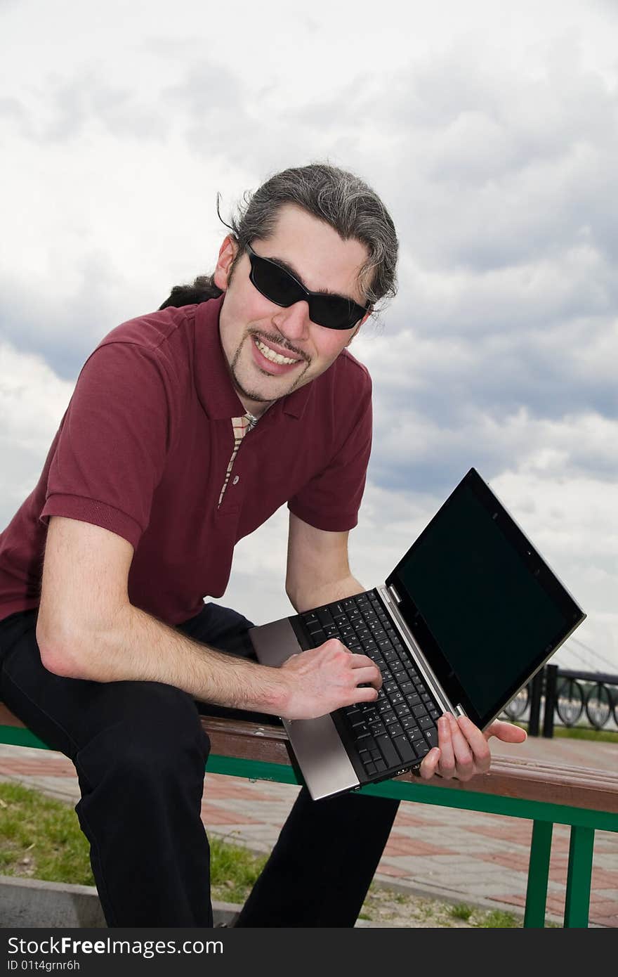 Young man sitting on a park bench with his laptop. Young man sitting on a park bench with his laptop