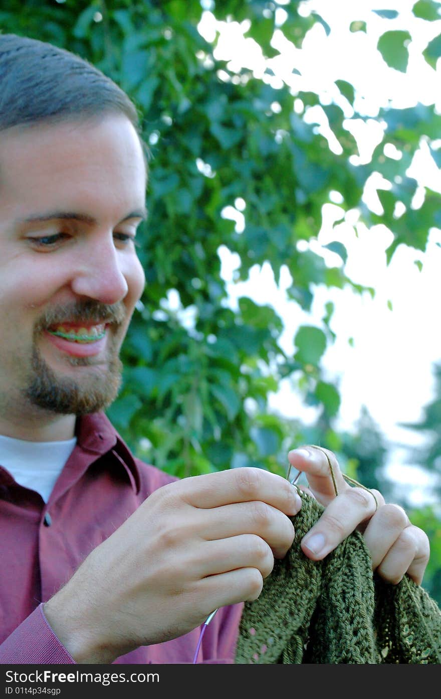 A man in a red shirt knits green lace with a tree in the background. Selective focus on the lace. A man in a red shirt knits green lace with a tree in the background. Selective focus on the lace.