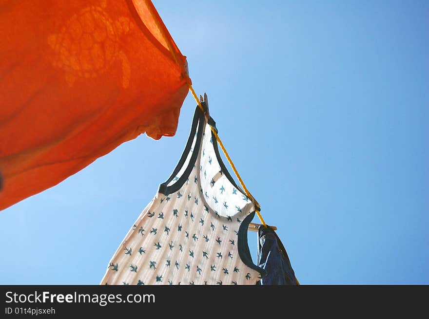 An orange t-shirt and a tank top with swallows on it dry in the breeze on a clothes line. An orange t-shirt and a tank top with swallows on it dry in the breeze on a clothes line.