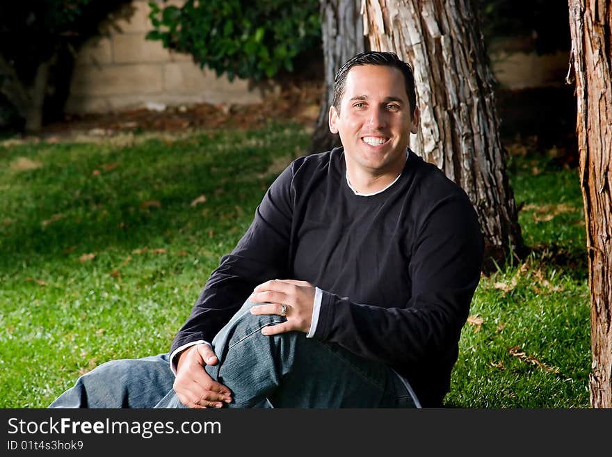 Portrait taken of a cheerful man sitting on the grass.