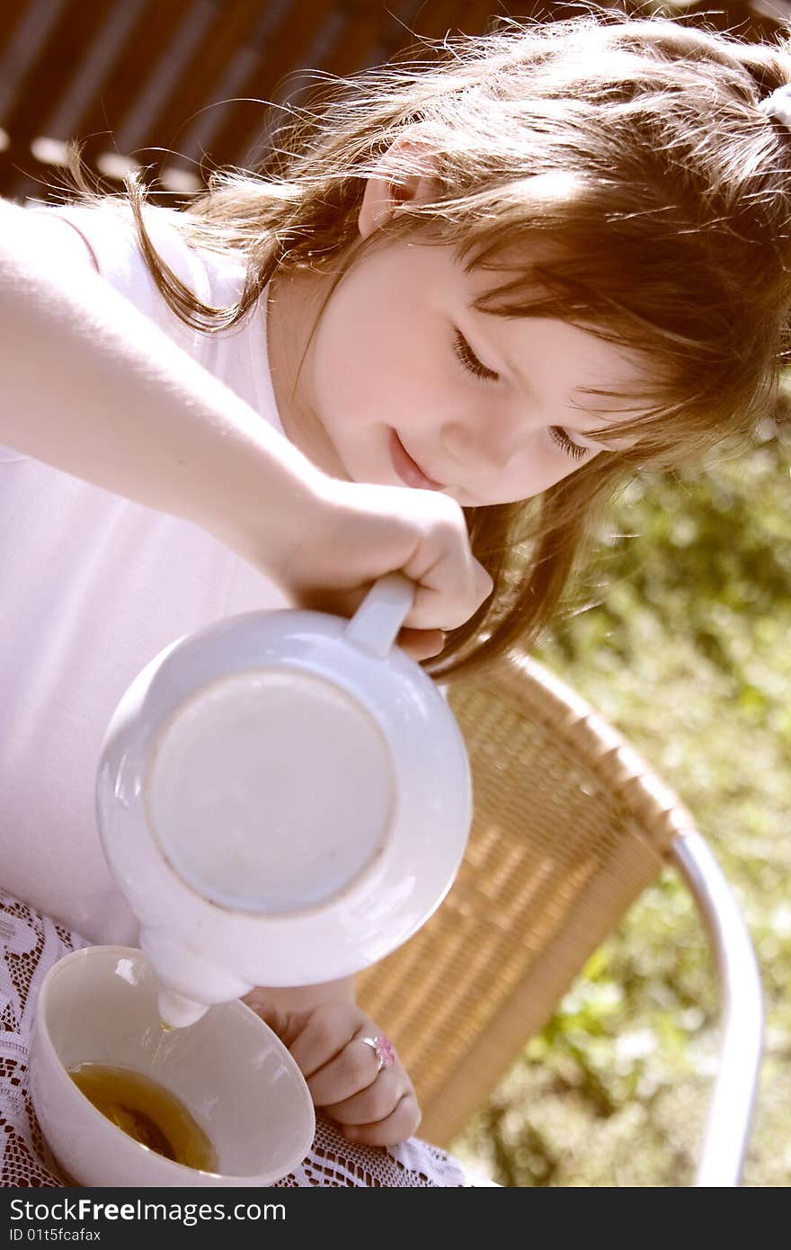 The beautiful  little girl pours hot tea in a cup