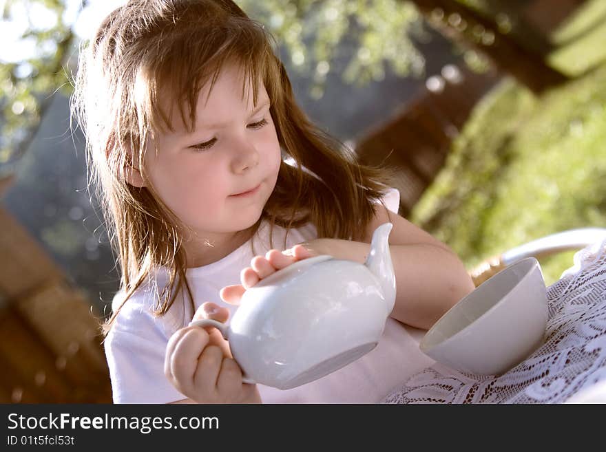 The beautiful  little girl pours hot tea in a cup