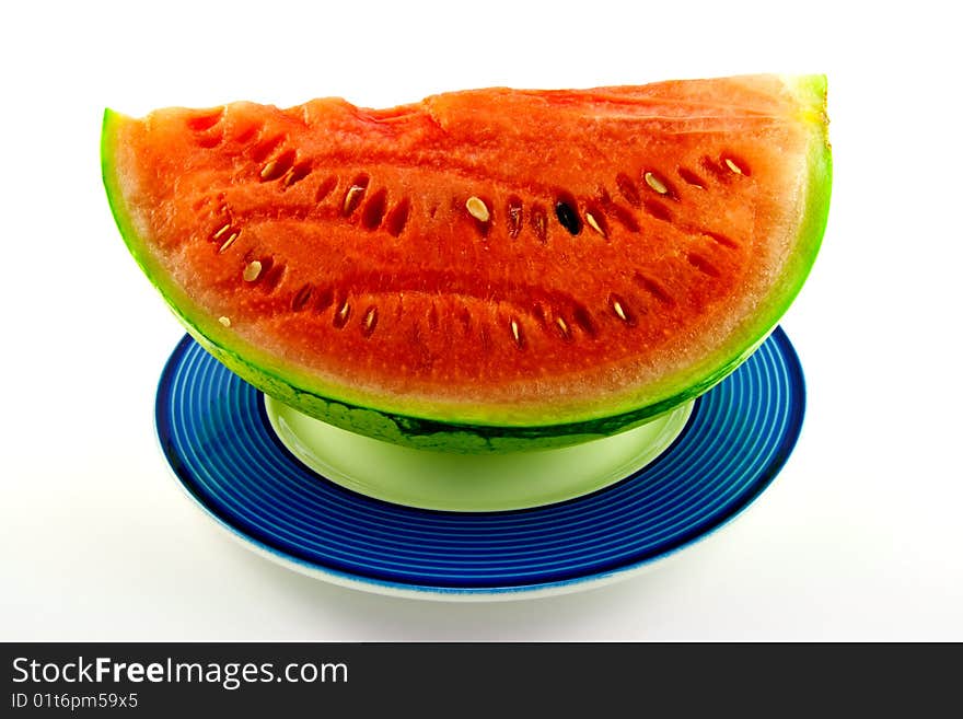 Slice of watermelon with green skin and red melon with seeds on a blue plate with a white background