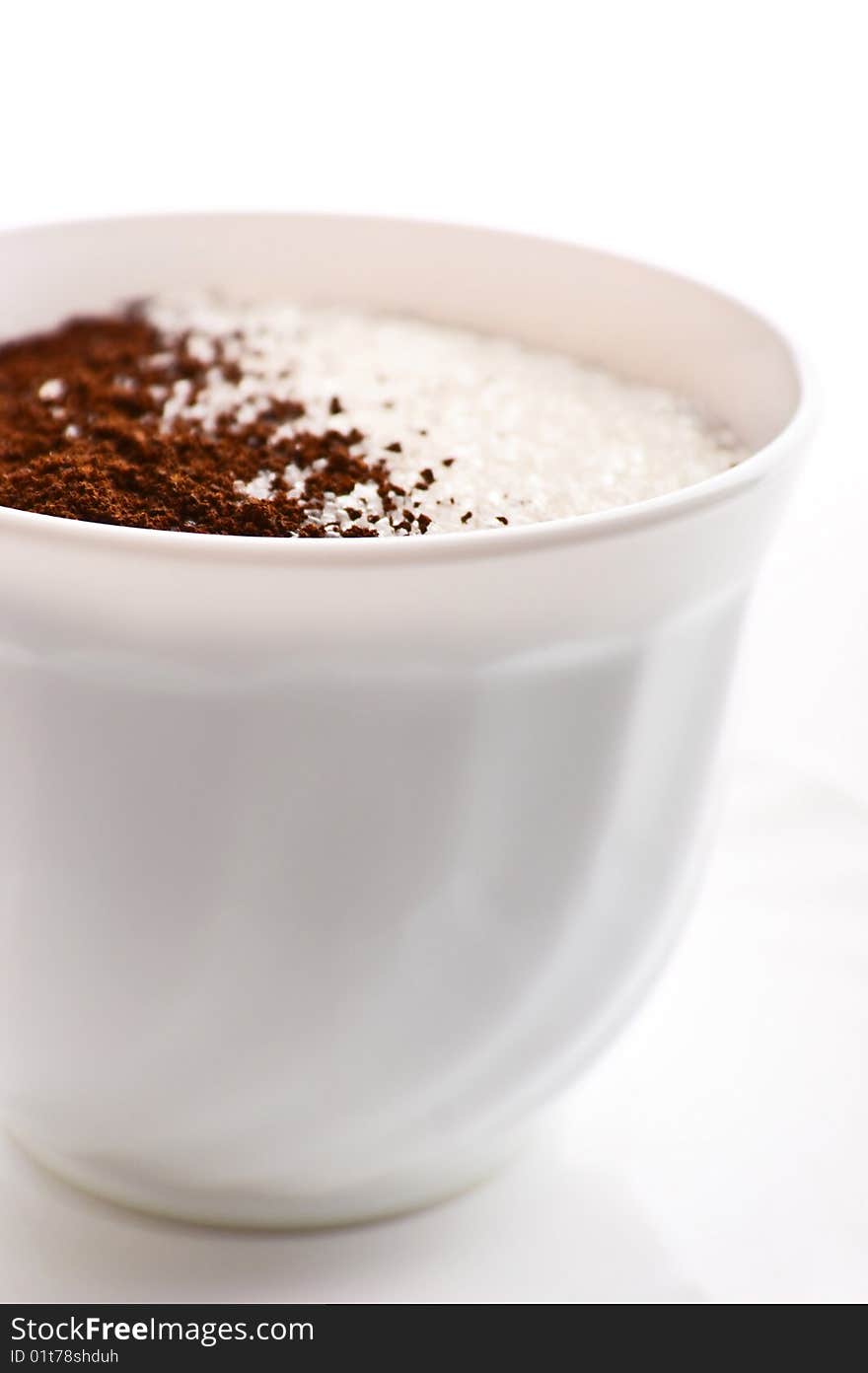 Cup with ground coffee inegrating into sugar is isolated over a white background. Cup with ground coffee inegrating into sugar is isolated over a white background