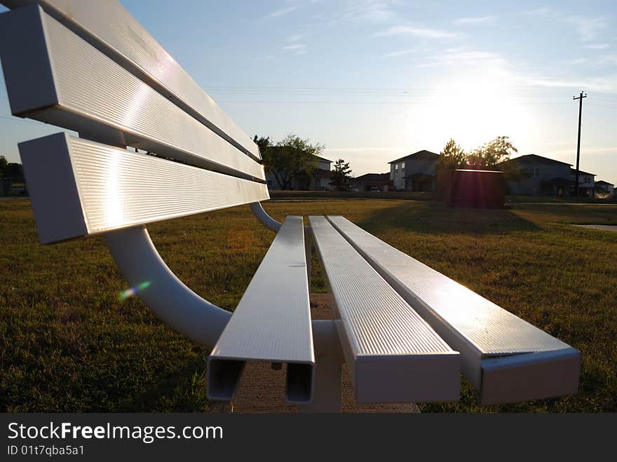 This park bench looks at a basketball court in Altus, OK.  The sun and houses in in the background light up the seat of the bench. This park bench looks at a basketball court in Altus, OK.  The sun and houses in in the background light up the seat of the bench.