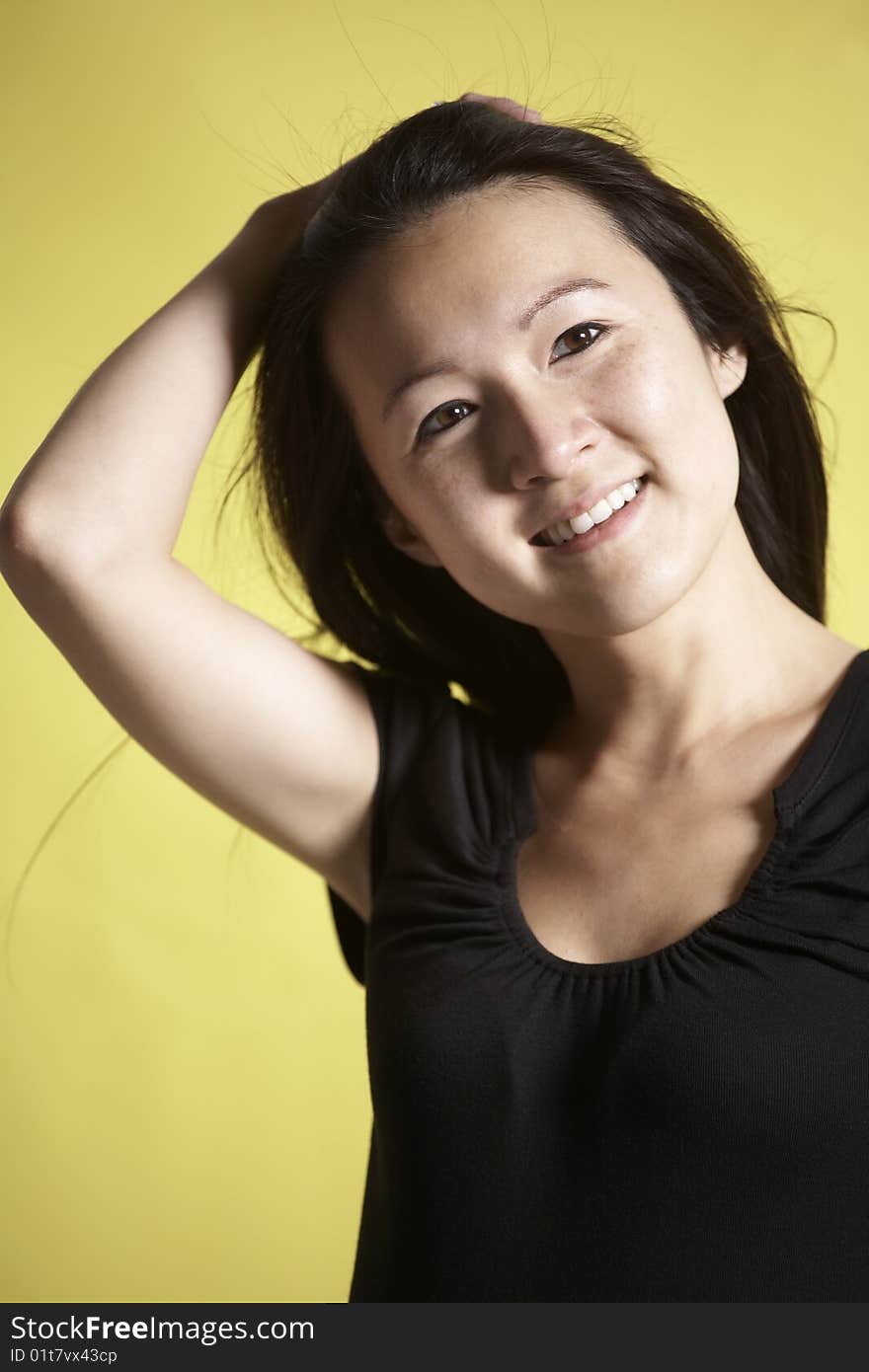 Young Asian woman standing against a yellow background pulls back her hair from her face. Young Asian woman standing against a yellow background pulls back her hair from her face.