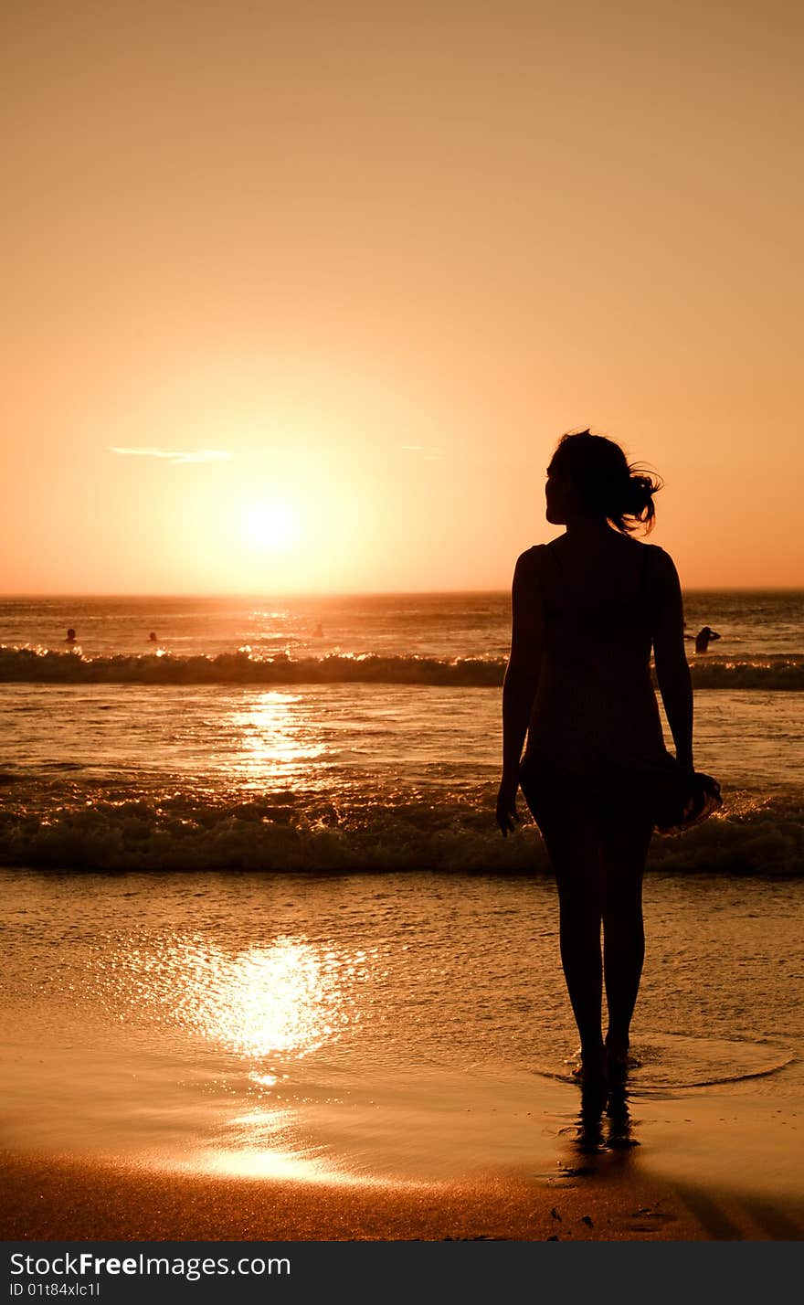 A pretty girl stands at the oceans edge looking at the setting sun. A pretty girl stands at the oceans edge looking at the setting sun.