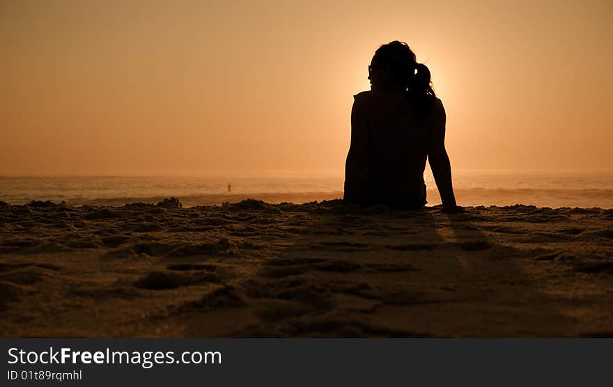 A pretty girl watches the waves at the beach during sunset. A pretty girl watches the waves at the beach during sunset.