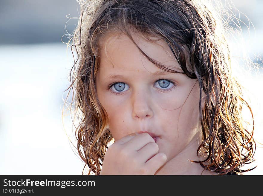 A child with hand up to her mouth eating crisps on a beach with crumbs all over her face. A child with hand up to her mouth eating crisps on a beach with crumbs all over her face