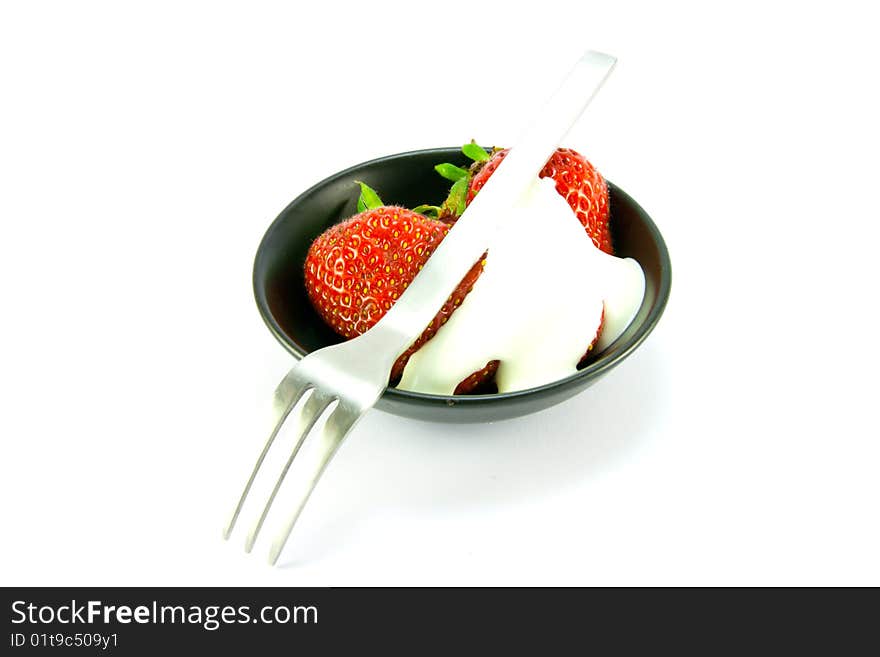 Sliced and whole red fresh strawberries with cream and small fork in a small black dish on a white background. Sliced and whole red fresh strawberries with cream and small fork in a small black dish on a white background