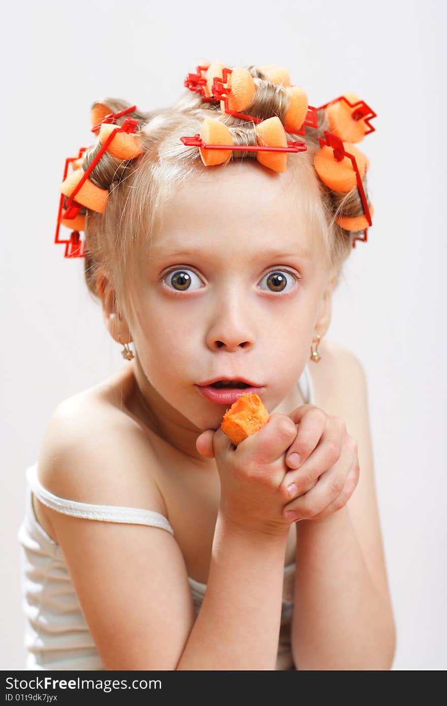 The girl with hair curlers gnaws carrots on a grey background. The girl with hair curlers gnaws carrots on a grey background