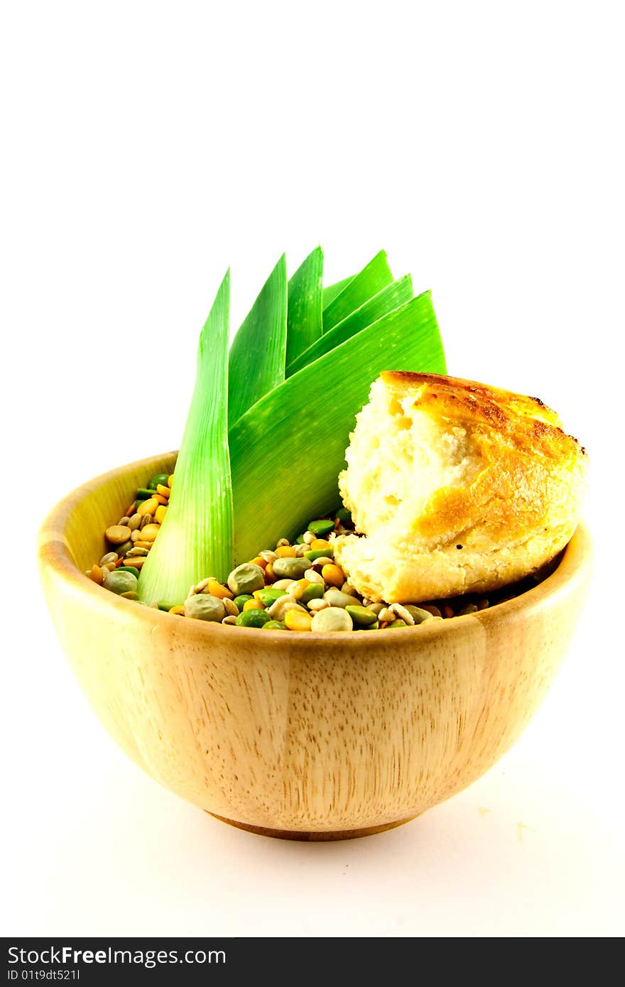 Wooden bowl of soup pulses with leek and crusty bread on a white background