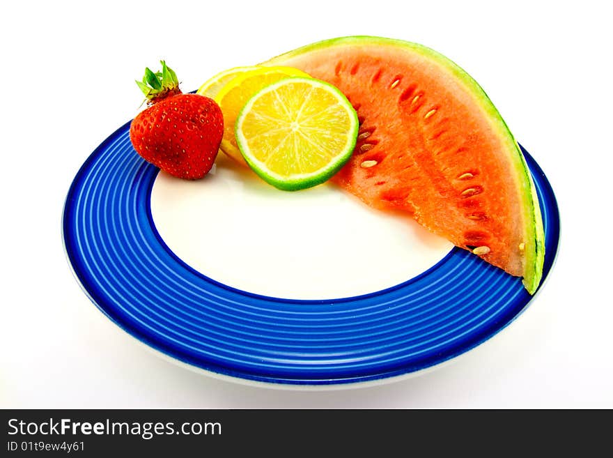 Slice of red juicy watermelon with lemon, lime and orange slices and single strawberry on a blue plate with a white background. Slice of red juicy watermelon with lemon, lime and orange slices and single strawberry on a blue plate with a white background