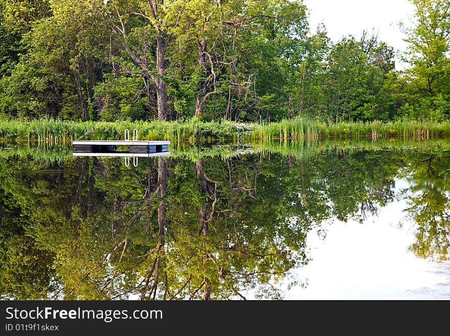 Swimming platform in the pond with trees reflecting in the pond. Swimming platform in the pond with trees reflecting in the pond.