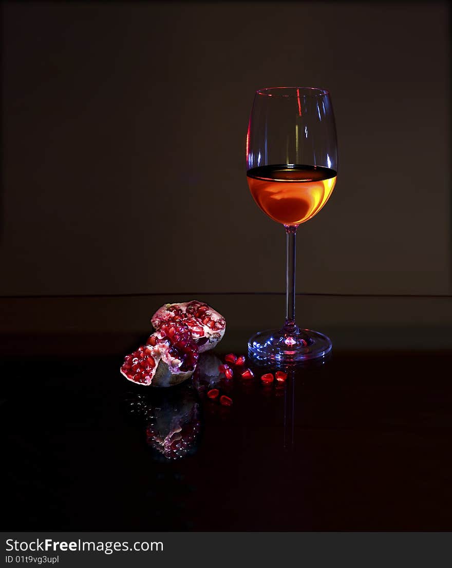 Glass with White wine and red pomegranate with reflection on dark background