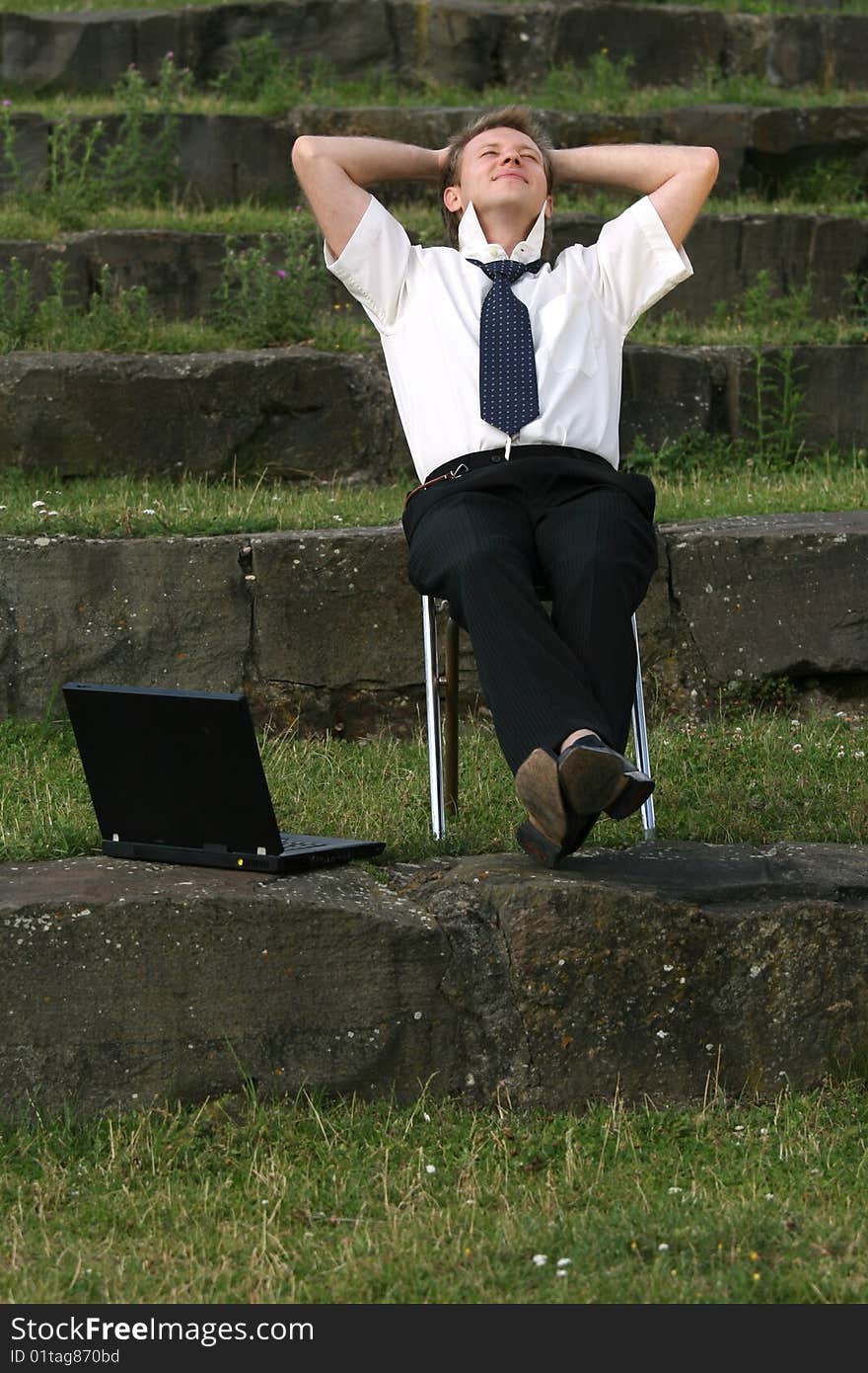 Relaxing businessman sitting outdoor with laptop