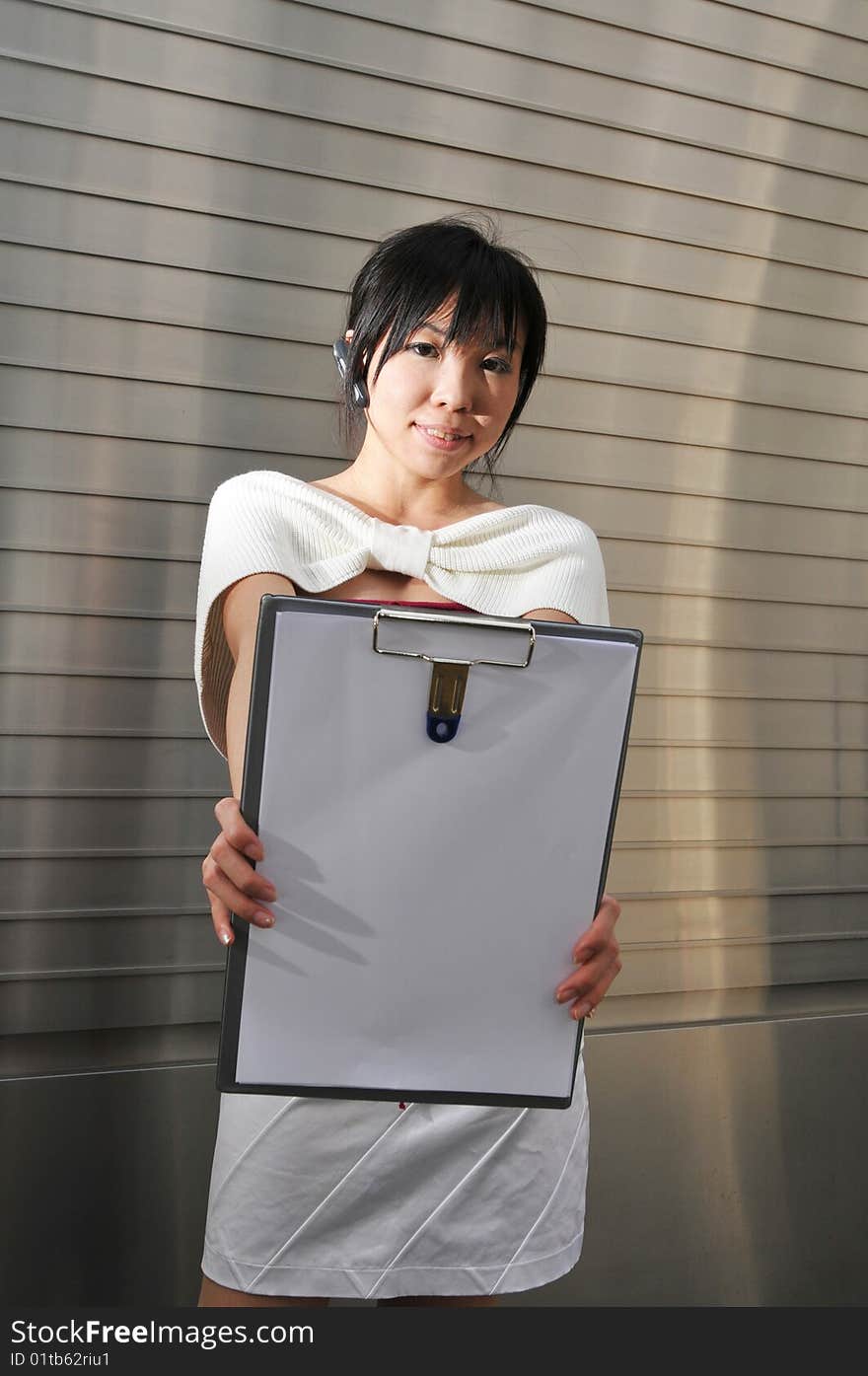 Beautiful young and modern Asian woman in the city showing a clipboard. Beautiful young and modern Asian woman in the city showing a clipboard.