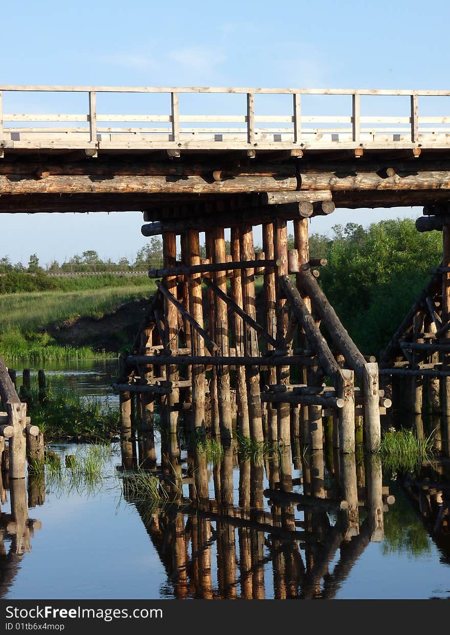 Wooden bridge and his reflection in water of river. Bridge footing. Wooden bridge and his reflection in water of river. Bridge footing.