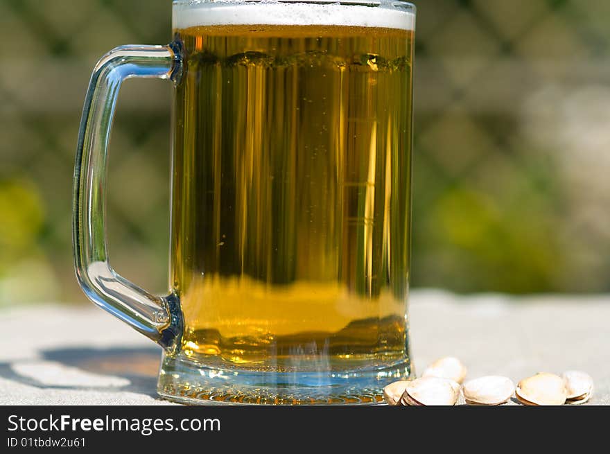 Full mug with beer on a table covered with a cloth and pistachios. Closeup. Full mug with beer on a table covered with a cloth and pistachios. Closeup