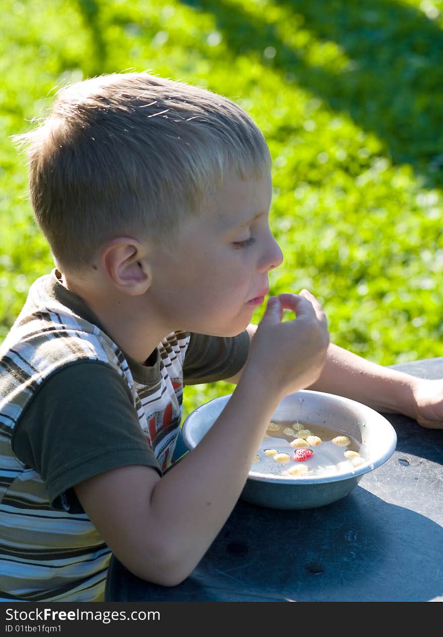 The child eats wild strawberry from a bowl behind table. The child eats wild strawberry from a bowl behind table.