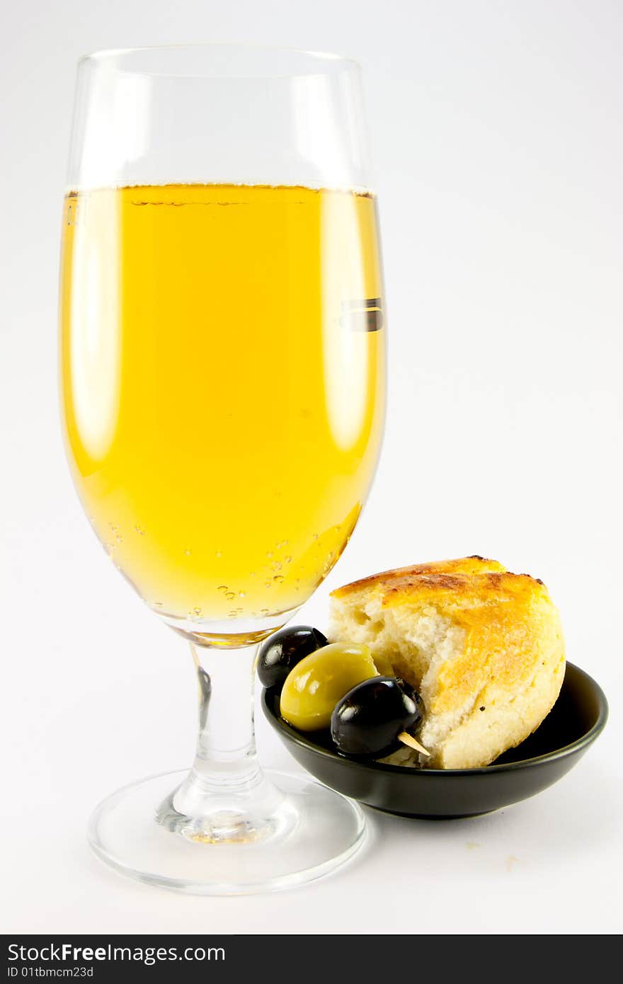 Glass of lager with three green olives and piece of crusty bread in a small black bowl on a plain background. Glass of lager with three green olives and piece of crusty bread in a small black bowl on a plain background