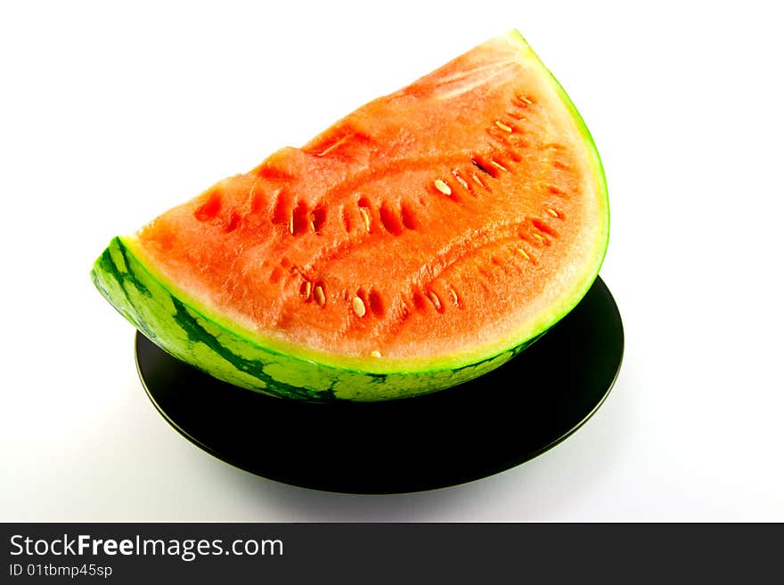 Slice of watermelon with green skin and red melon with seeds on a black plate with a white background. Slice of watermelon with green skin and red melon with seeds on a black plate with a white background