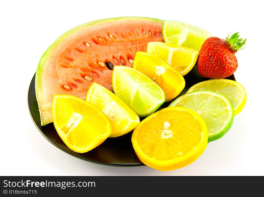 Slice of watermelon with lemon, lime and orange segments and single red strawberry on a black plate with a white background. Slice of watermelon with lemon, lime and orange segments and single red strawberry on a black plate with a white background