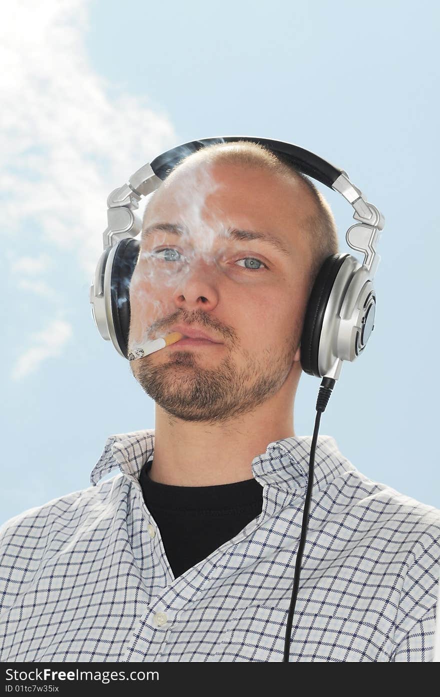 DJ with headphones smoking in front of blue sky. DJ with headphones smoking in front of blue sky