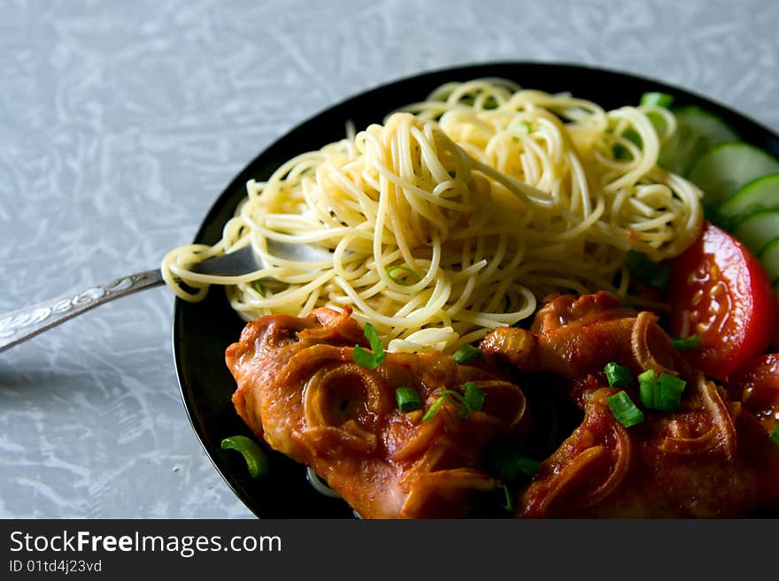 A plate with chicken wings, spaghetti and pieces of tomatoes and cucumbers. A plate with chicken wings, spaghetti and pieces of tomatoes and cucumbers