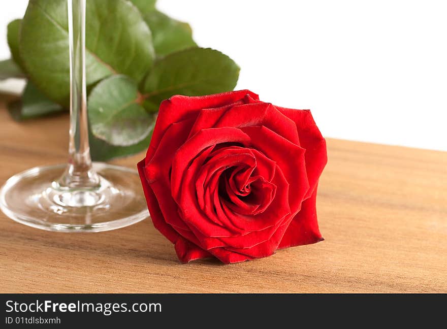 A red rose and a wine glass on a wooden bottom isolated on white background. A red rose and a wine glass on a wooden bottom isolated on white background