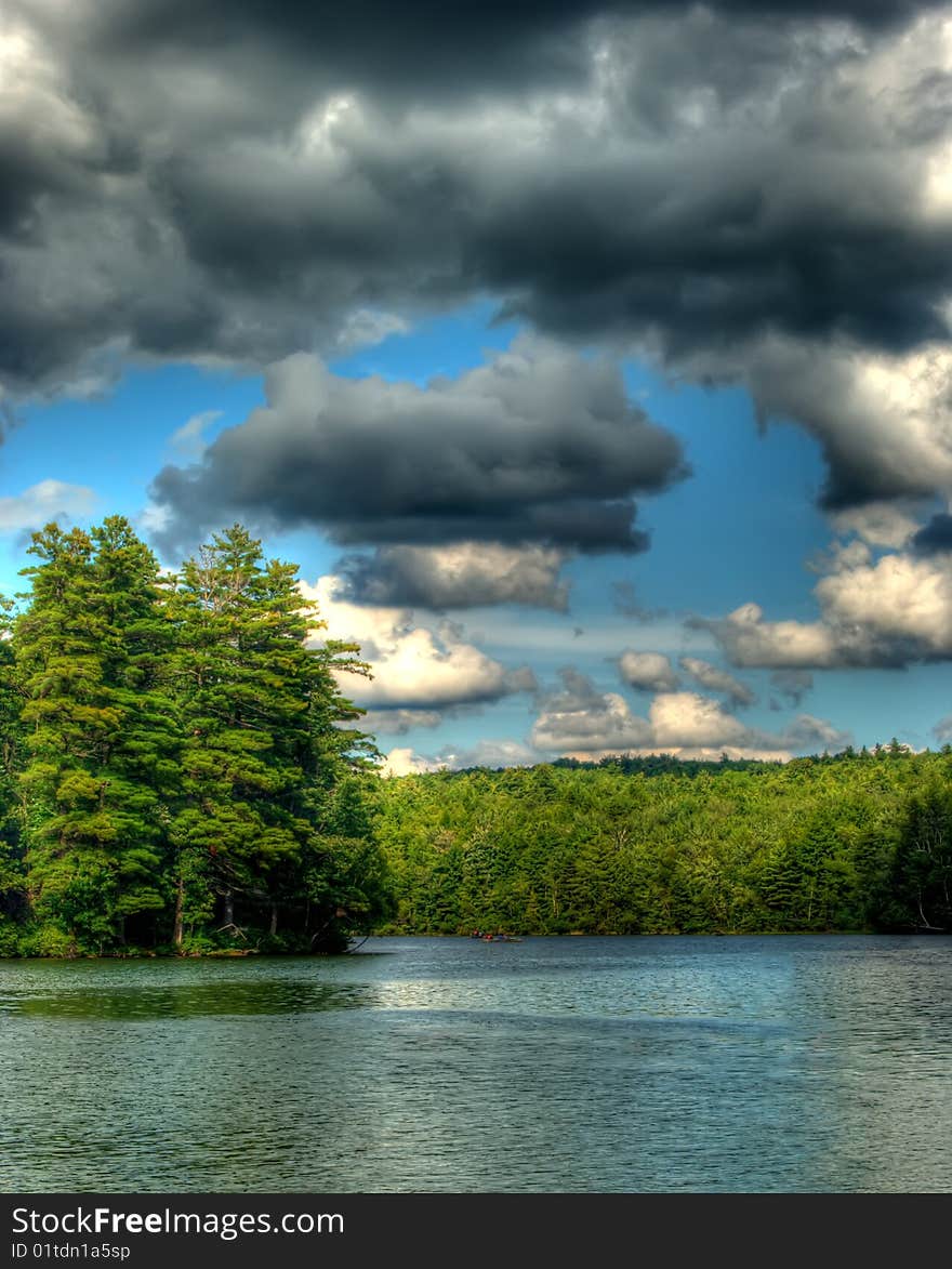 Cumulus clouds in a blue sky over a lake that is surrounded by trees. Cumulus clouds in a blue sky over a lake that is surrounded by trees.