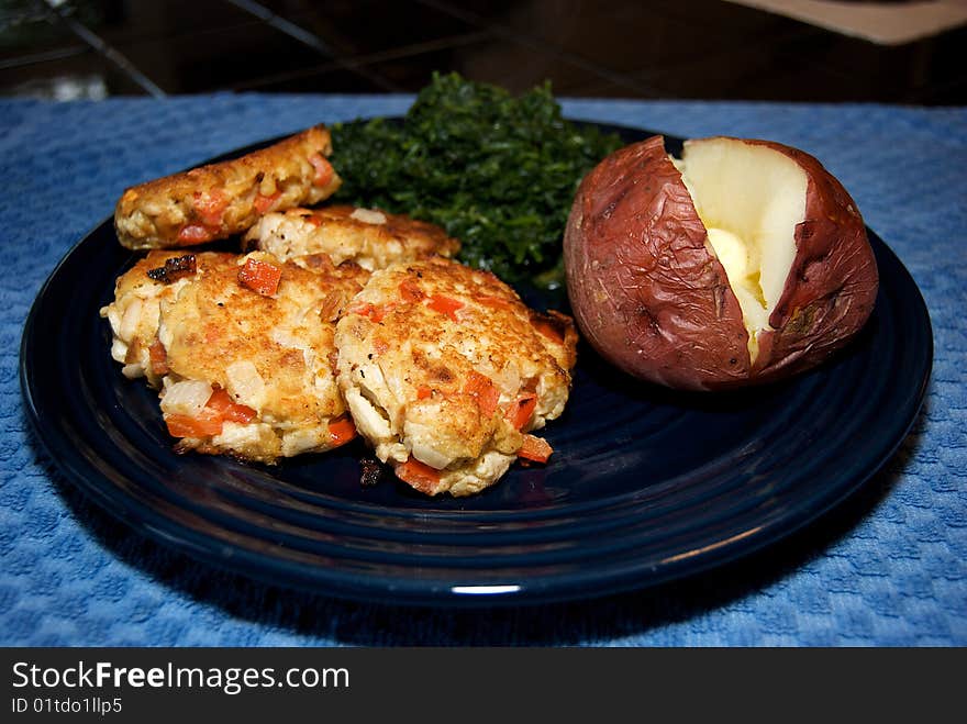 Crab cakes plated with a red potato and spinach. Crab cakes plated with a red potato and spinach.