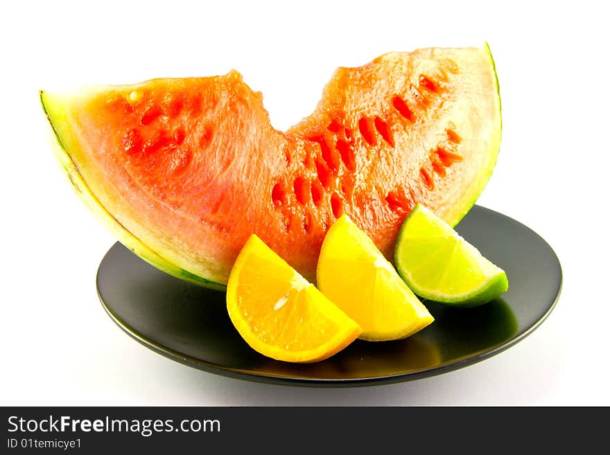 Slice of red juicy watermelon with a wedge of lemon, lime and orange on a black plate with a white background. Slice of red juicy watermelon with a wedge of lemon, lime and orange on a black plate with a white background