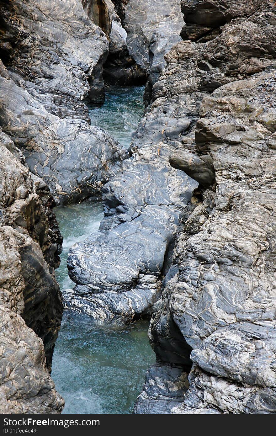 Narrow seething mountain stream flows among blue striped rocks in Alps. Narrow seething mountain stream flows among blue striped rocks in Alps