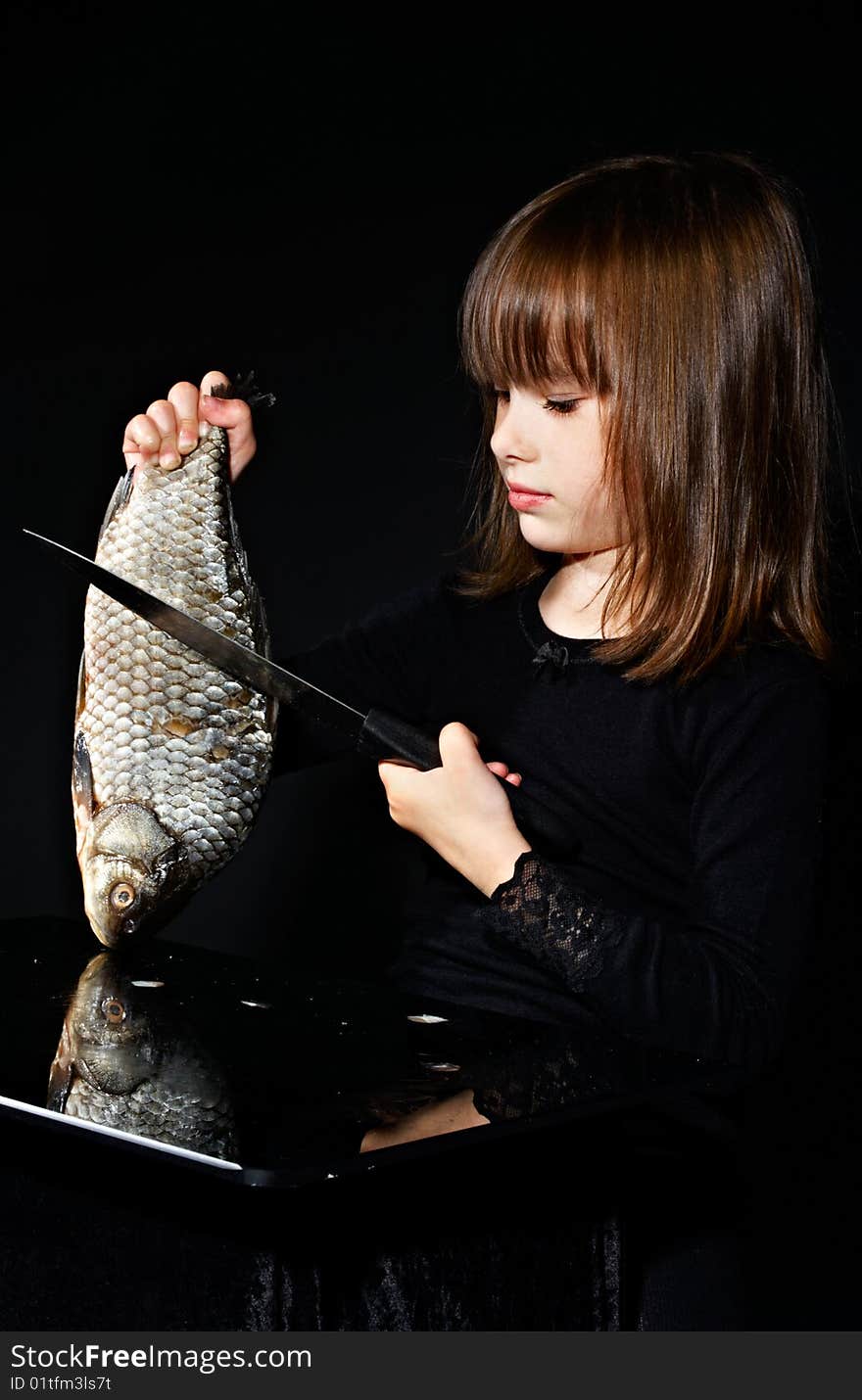 Little girl cuts raw fish. Little girl cuts raw fish