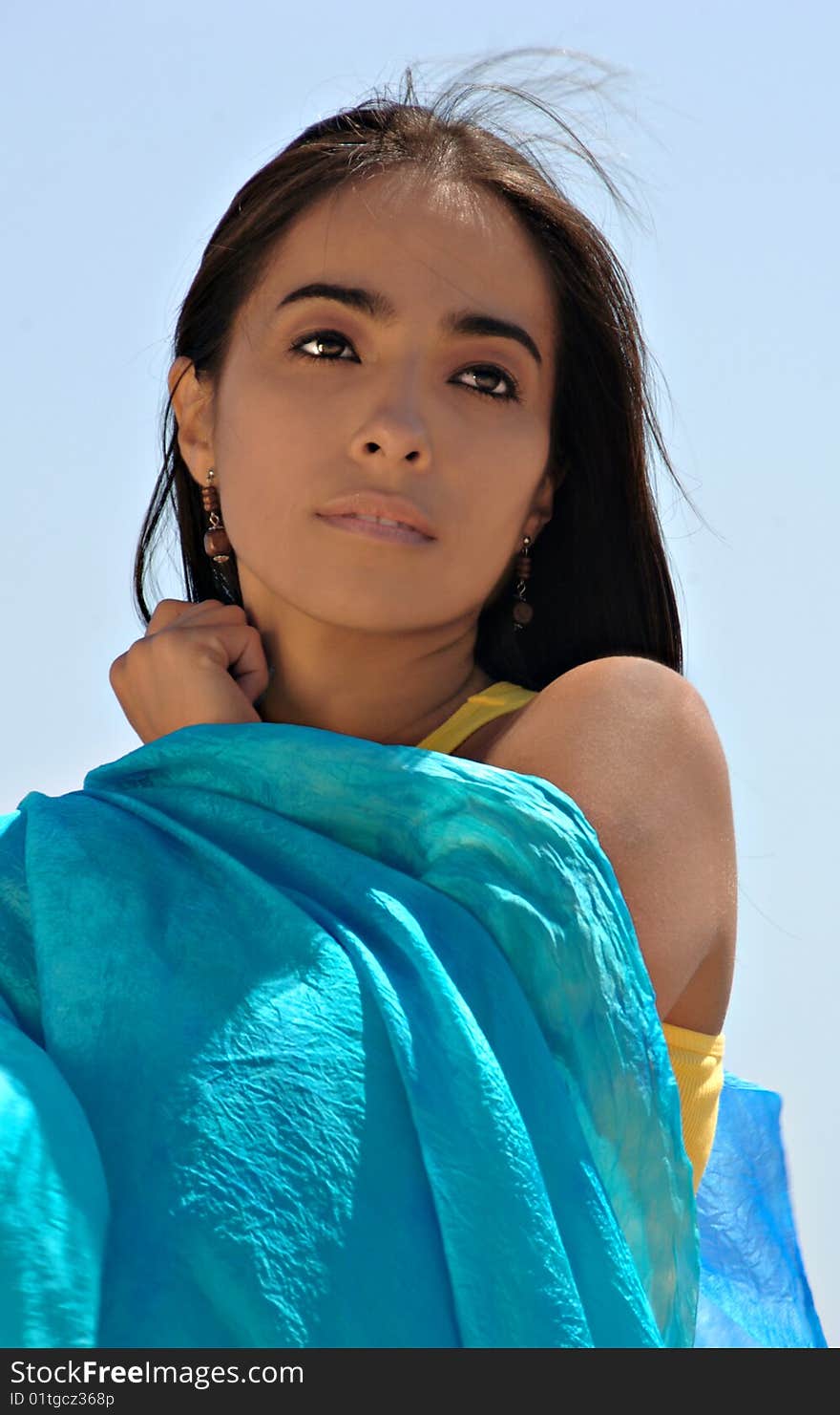 Young Hispanic woman with a blue scarf against a blue sky. Young Hispanic woman with a blue scarf against a blue sky.