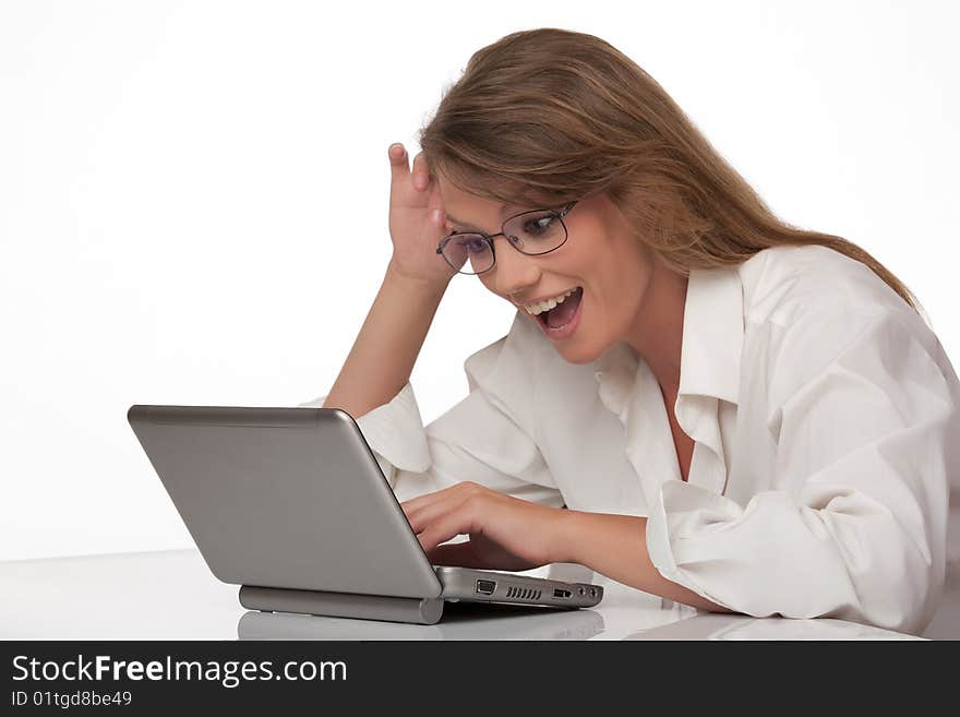 The modern young woman sits at a table with a personal computer, joyfully smiling, looks at the screen of a computer. The modern young woman sits at a table with a personal computer, joyfully smiling, looks at the screen of a computer