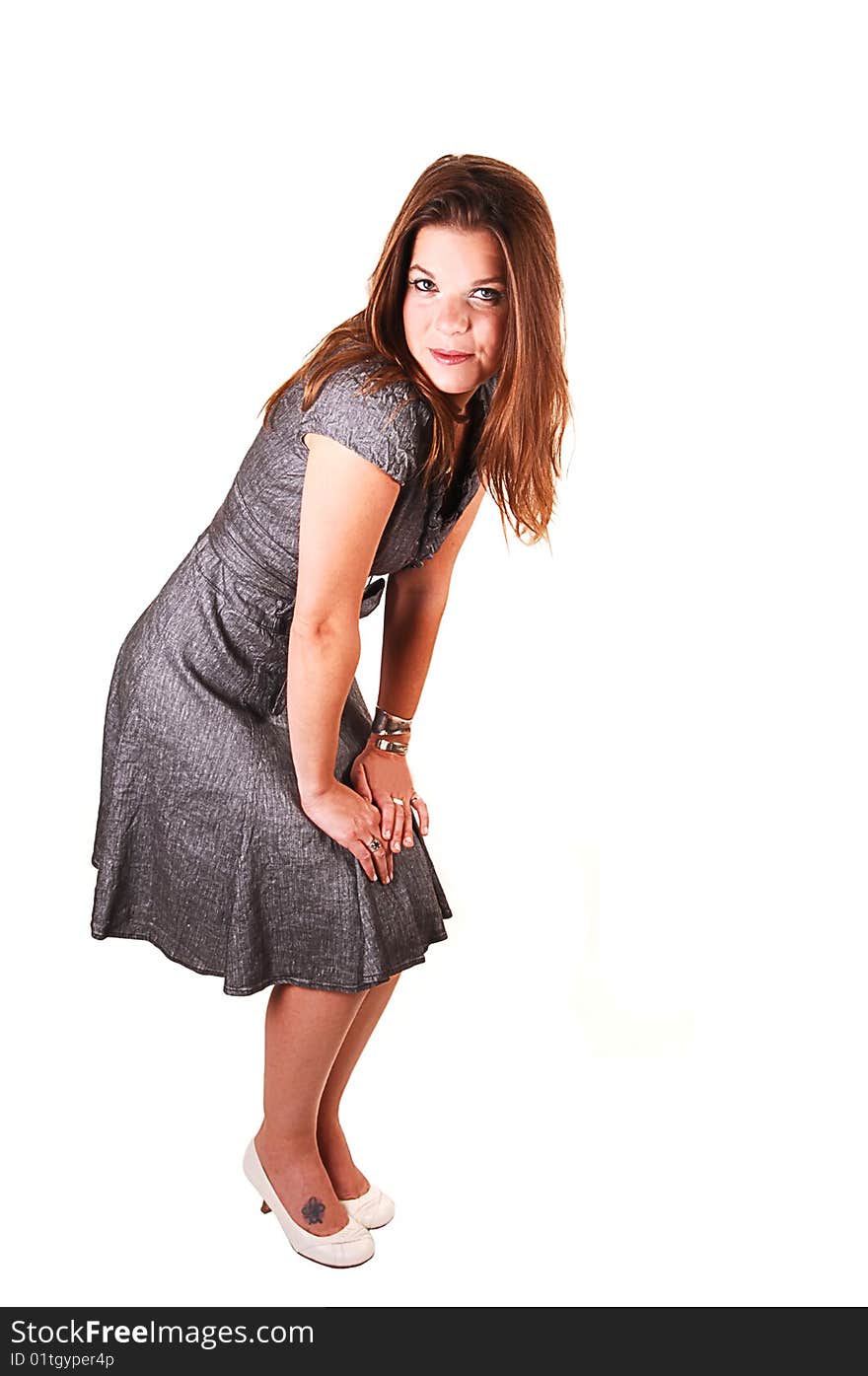 Young lovely girl in a gray dress hands on her knees and looking in the camera, standing in the studio for white background. Young lovely girl in a gray dress hands on her knees and looking in the camera, standing in the studio for white background.