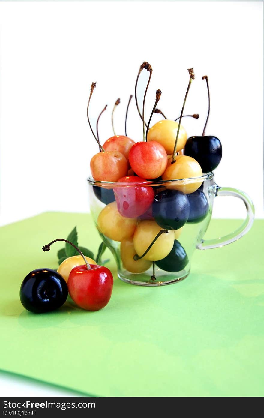 Sweet cherries in a glass cup, arranged with three cherries on a green napkin, vertical