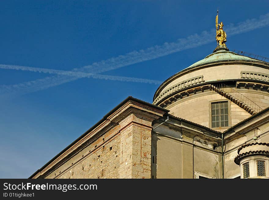 Old building with a golden statue on top and sky with flight trails in the background. Old building with a golden statue on top and sky with flight trails in the background