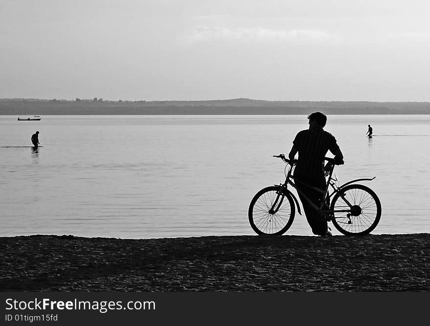 Cyclist on the shore of the lake at sunset. Bathers in the background. Cyclist on the shore of the lake at sunset. Bathers in the background.