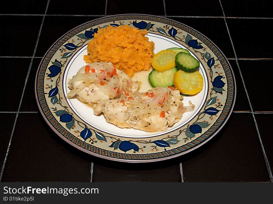 Chicken, mashed sweet potatoes and summer squash and zucchini, plated on a black tile table. Chicken, mashed sweet potatoes and summer squash and zucchini, plated on a black tile table.