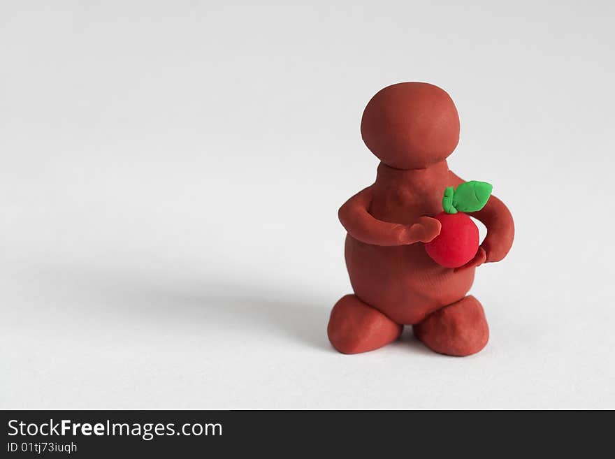 Plasticine man keeping a red apple over grey background