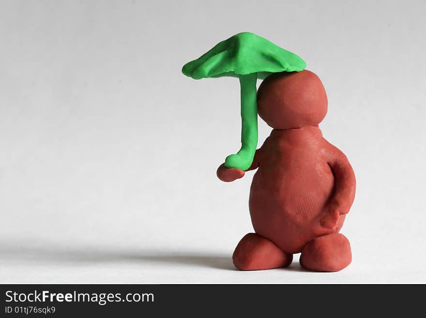 Plasticine man under the green umbrella over grey background